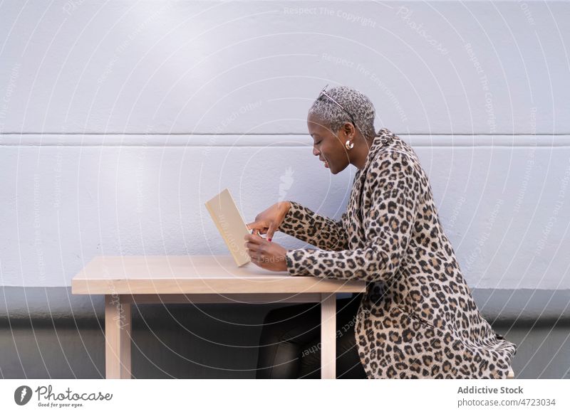 Black woman reading letter from cafe terrace street style outfit city trendy female african american black table lady pastime cafeteria apparel content focus