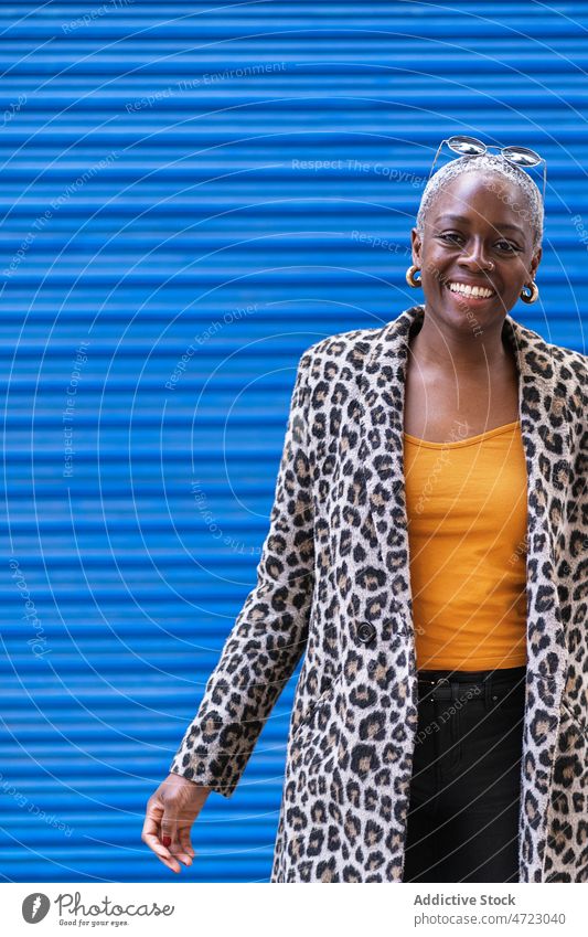 Positive black woman near blue wall street style appearance outfit trendy city urban garment smile african american female glad content happy positive coat