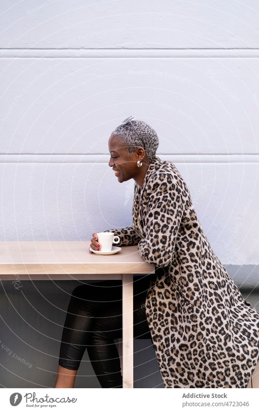 Optimistic black woman in outdoor cafe terrace coffee break playful pastime street needlework appearance african american short hair female city lady hot drink