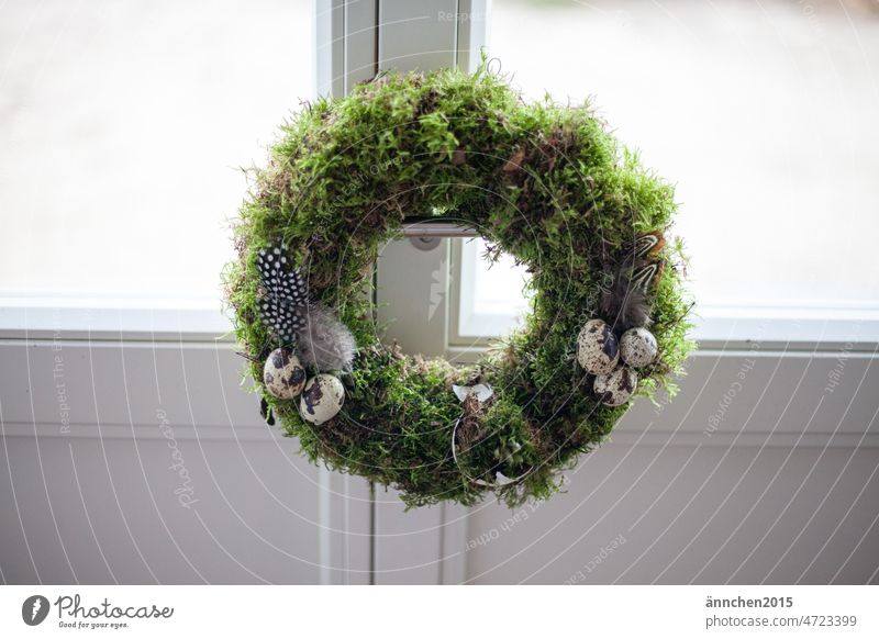 An Easter wreath made of moss decorated with eggs and feathers hangs on a white door Wreath Spring celebration celebrations Seasons DIY Wreath binding Moss