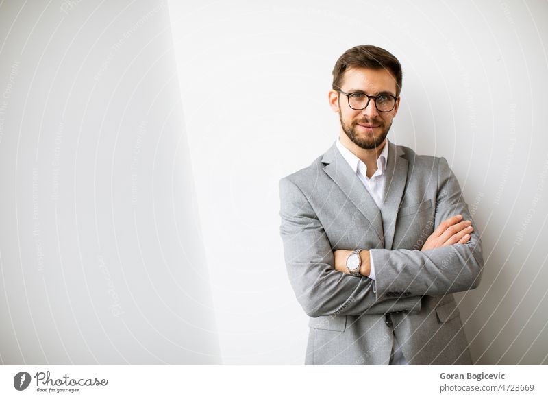 Young modern businessman standing by the wall in the office beard company corporate employee eyeglasses financial handsome indoors job leadership male manager
