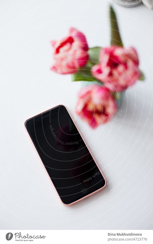 Mobile phone and three pink tulips in a small vase on white background, smartphone and home decor spring background with flowers Technology mobile Gift