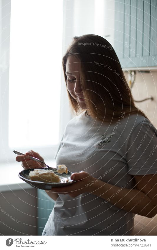 young woman at home eating dessert in the morning smiling to new day standing in the kitchen good morming candid real people lifestyle fresh attractive