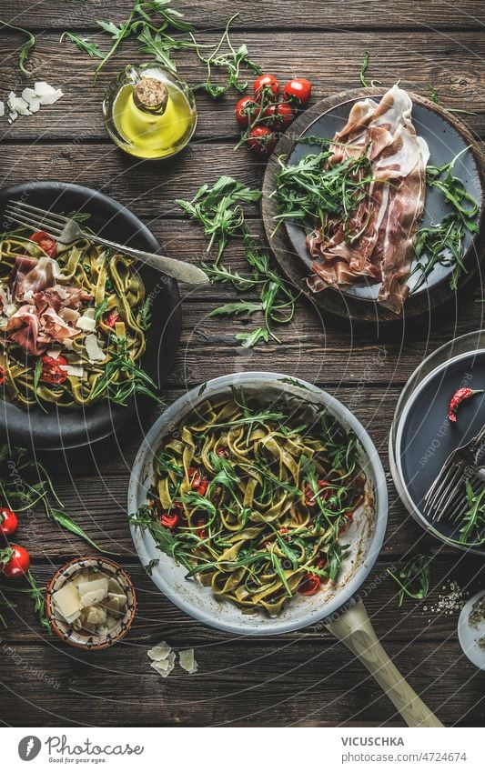Green cooked pasta in cooking pan with Parma ham, arugula, tomatoes and cheese italian food background green parma ham rustic wooden kitchen table homemade
