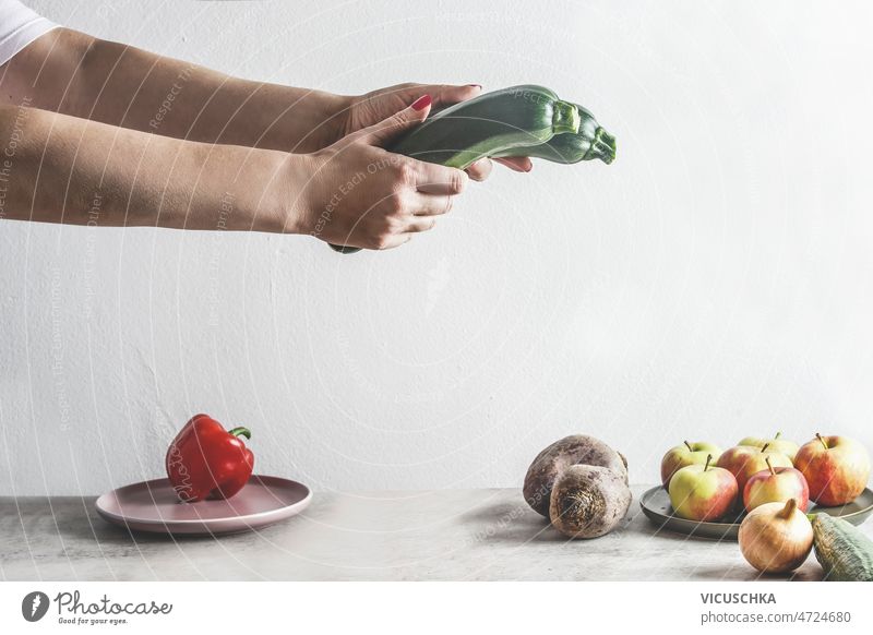 Woman hands holding two green courgettes about grey kitchen table with fruits and vegetables woman white wall background healthy lifestyle front view apples