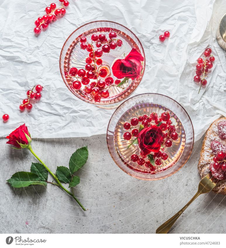 Close up of two champagne glasses with red currants and rose flowers close up petals white table golden fork pastry romantic drink concept decoration