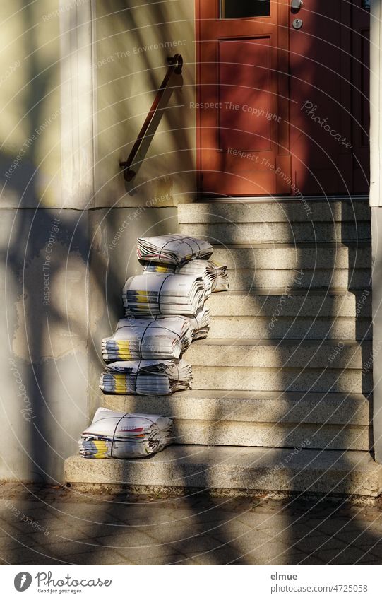 Several bundles of hot-off-the-press daily newspapers with color-coded articles on the Ukraine war lie ready for delivery on the front steps of an old apartment building / Reporting / Print media