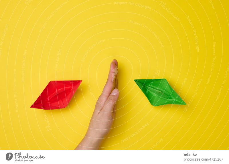 female hand between paper boats on a yellow background, the concept of reconciliation of the parties, the search for compromises. The role of the negotiator in the dialogue