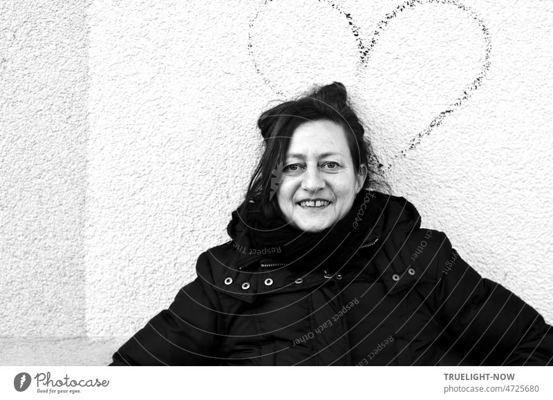 bit.it lion's heart - the brave woman is perhaps amused by the photographer. Warmly wrapped up to the chin with wildly pinned up hair she stands resolutely smiling frontally to the camera directly in front of the big heart on the already known white wall