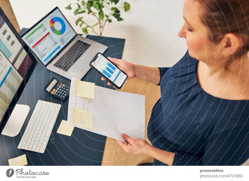 Businesswoman working with financial data on charts and tables on smartphone and computer. Woman entrepreneur looking at sale stats business office graph