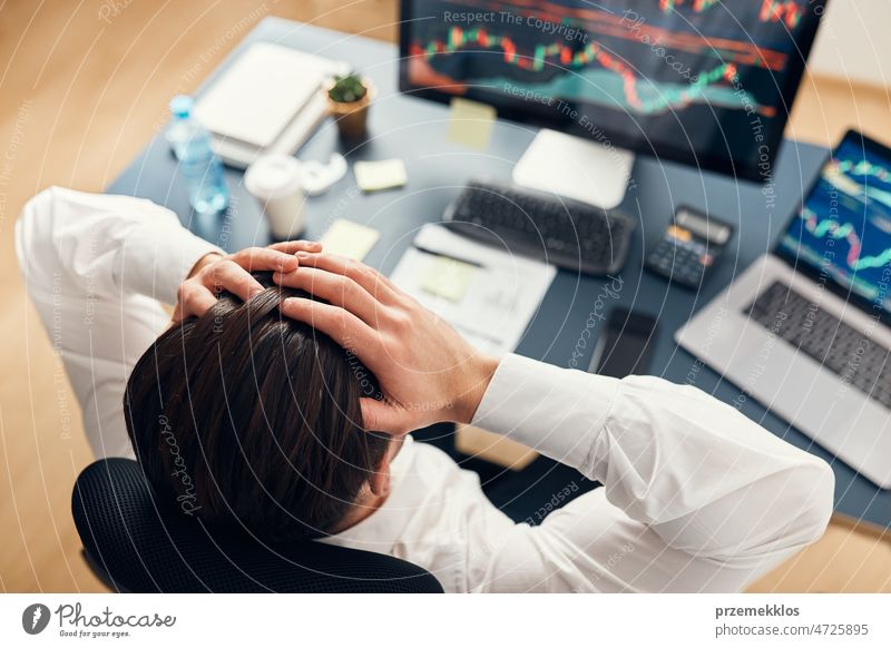 Worried businessman looking at charts stressed by news from stock market. Investor lost money online. Man analyses loss and profit. Businessman investing stocks online. Man working with stock chart data