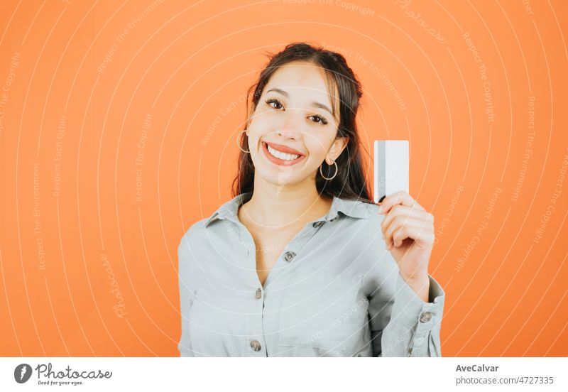 Young woman holding a mock up credit card showing it to camera while smiling, business and freelance concept. Blue tone color background, expression of normal people. Mockup concept with people