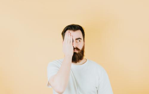 Handsome hipster bearded covering one eye with his hand and looking away from camera. Young man attitude funny. Soft tone color background, expression of normal people. Mockup concept with people