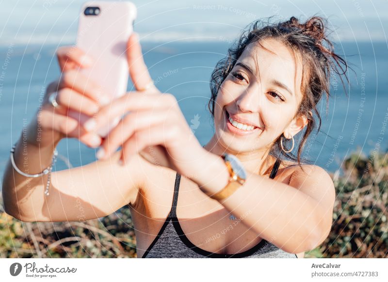 Young woman outdoors on sport clothes taking a selfie for social network after training. Carefree, positive and freedom concept. Healthy lifestyle doing exercise outdoors. Happy attitude