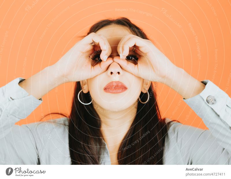 Young woman looking at something doing binoculars with his hand playfully. Young woman attitude. Orange tone color background, expression of normal people. Mockup concept with people