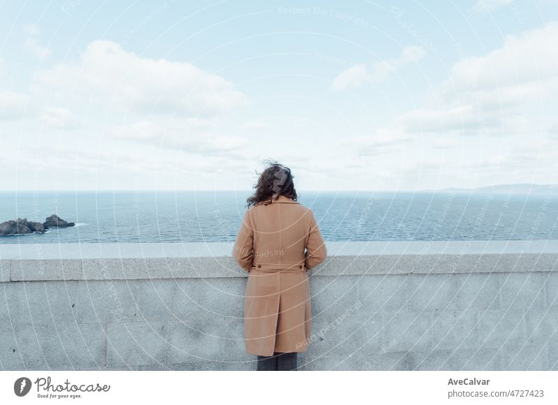 Young woman on a brown coat looking to the horizon, mental health concept. Bright sky, solitude and reflexion. Looking to the future person ocean young female