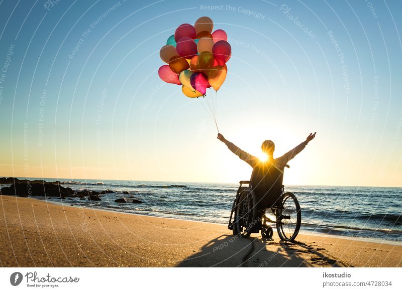Anything is possible woman wheelchair happy beach balloons sunset handicapped hands up celebrate happiness arms healthcare joy leisure success motivation