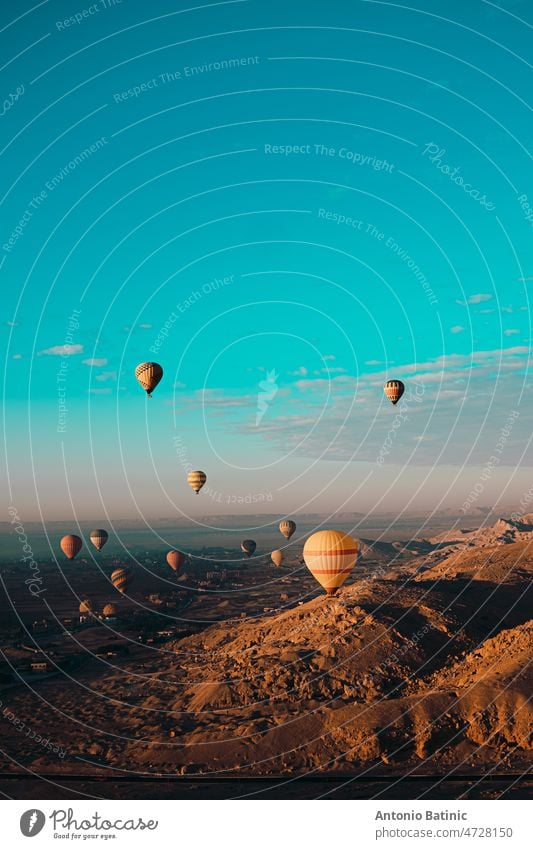 Amazing vertical shot of dozens of hot air balloons flying around the luxor egypt area. Desert orange area early in the morning. Bright blue sky flame sunny