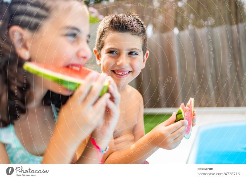 Two funny kids eating watermelon at the the edge of the pool on a summer day boy bright child childhood children cute enjoy expression food fresh fruit garden