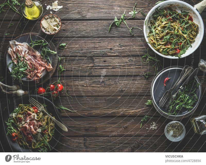 Green pasta on plates, ingredients and kitchen utensils with Parma ham, tomatoes, arugula green parma ham cheese olive oil italian food background frame