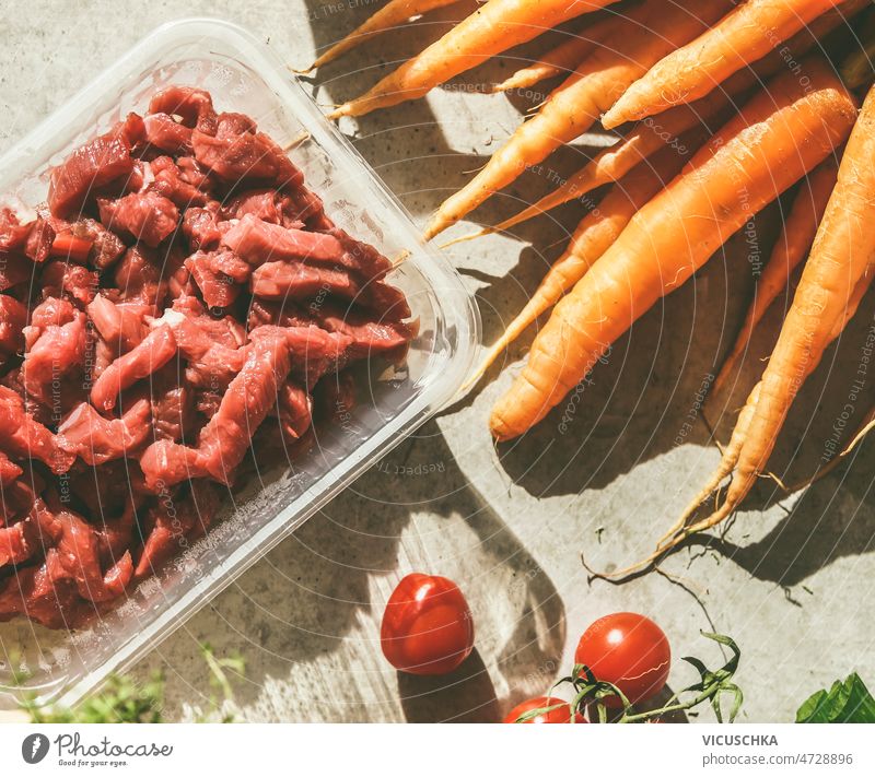 Close up of raw sliced meat in plastic container, carrots and tomatoes close up concrete kitchen table sunlight cooking preparation fresh ingredients home