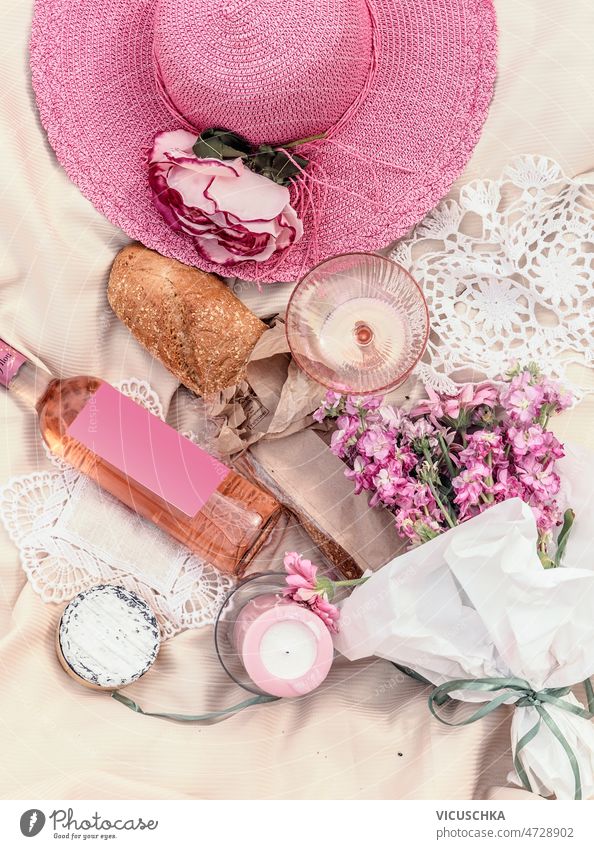 Pink colored picnic concept with sun hat, rose wine bottle, candles, flowers, baguette cheese pink beige blanket romantic summer idea food drink top view