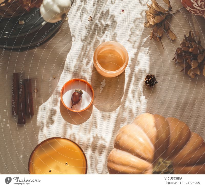 Cozy still life with candles, pumpkin, cinnamon sticks and autumn leaves at beige table blanket with sunlight cozy seasonal decoration shadow top view