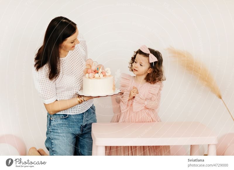 A young mother and her little daughter celebrate their birthday with a cake. mom table celebrating home gift relationship beautiful kid woman girl portrait