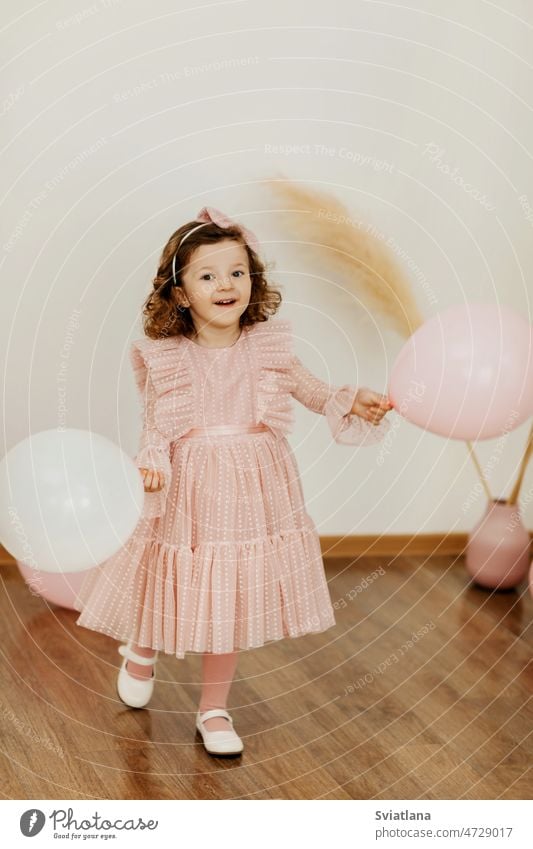 A charming little girl with balloons on her birthday has fun and laughs baby dress balls cute smile pink beautiful happy sweet light happiness child kid party