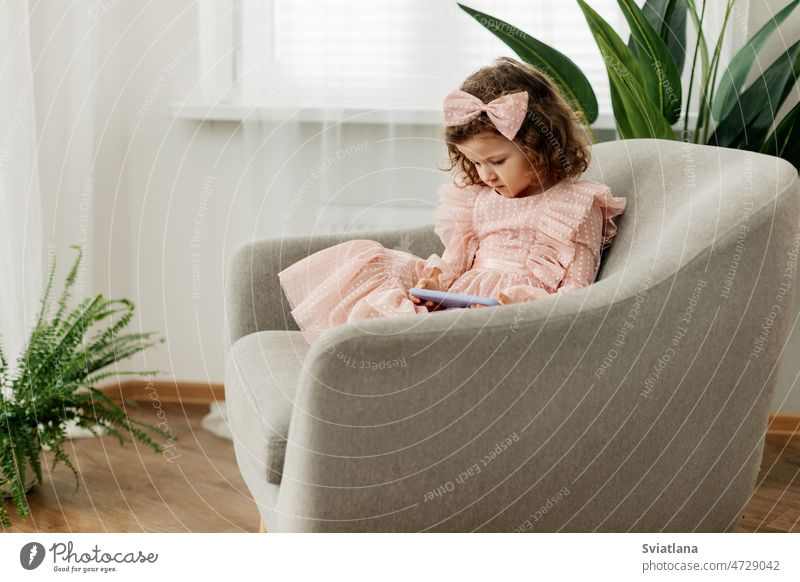A little girl is sitting in a chair playing a game on her phone or watching cartoons baby smartphone technology child portrait lifestyle childhood communication