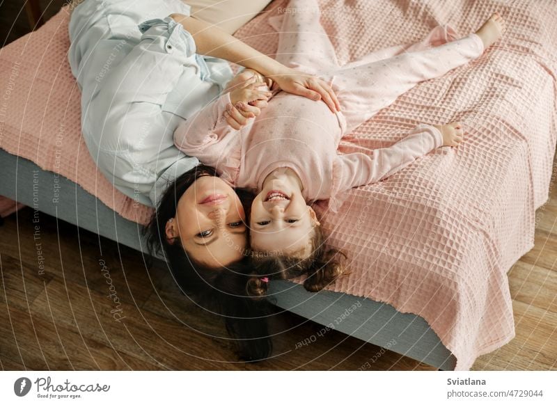 Mom and daughter are lying on the bed and smiling. Mom and baby are having fun on the bed. Happy loving family mom playing young girl child bedroom happy mother