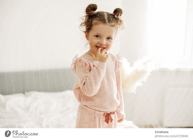 Portrait of a happy girl standing on the bed in the bedroom in the morning after waking up baby one looking bright child cute kid home small childhood portrait