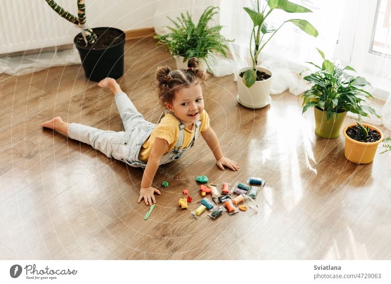 A charming little girl sculpts from colored plasticine on the floor. Home schooling, creative leisure with children baby play home making childrens creativity