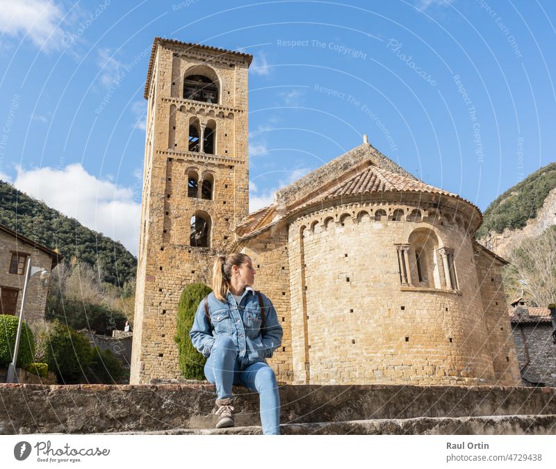 Beautiful young woman sitting in beautiful medieval village.Relaxed female visiting Beget with the romanesque church of Saint Christopher on background spanish