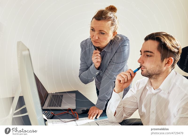 Two business people discussing financial data looking at computer screen. Businesswoman talking to young male coworker in office. People entrepreneurs having conversation working together