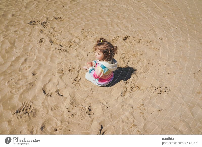 Young toddler playing with the sand at the beach alone enjoy summer explore parenting freedom happy rainbow happiness scene curly hair kid child baby childhood
