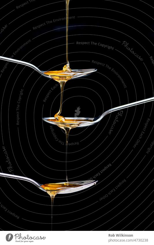 fresh honey pouring over three spoons amber close up view closeup concept copy space cutlery delicious drip dripped dripping drop falling flow flowing fluid