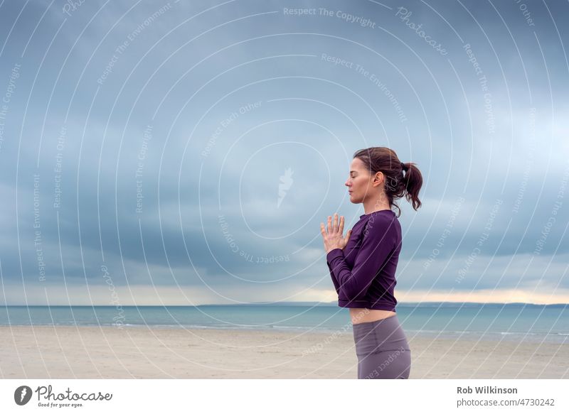Cropped view of woman standing meditating and practicing yoga by the sea. Fitness and mental health concept. adult attractive beach cloud copy space female fit