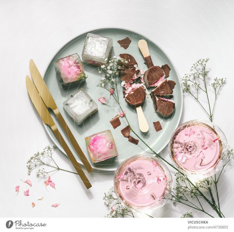 Ice cream popsicles with chocolate on plate with gypsophila,  wine glasses with rose wine ice cream ice cubes golden knifes white table summer setting
