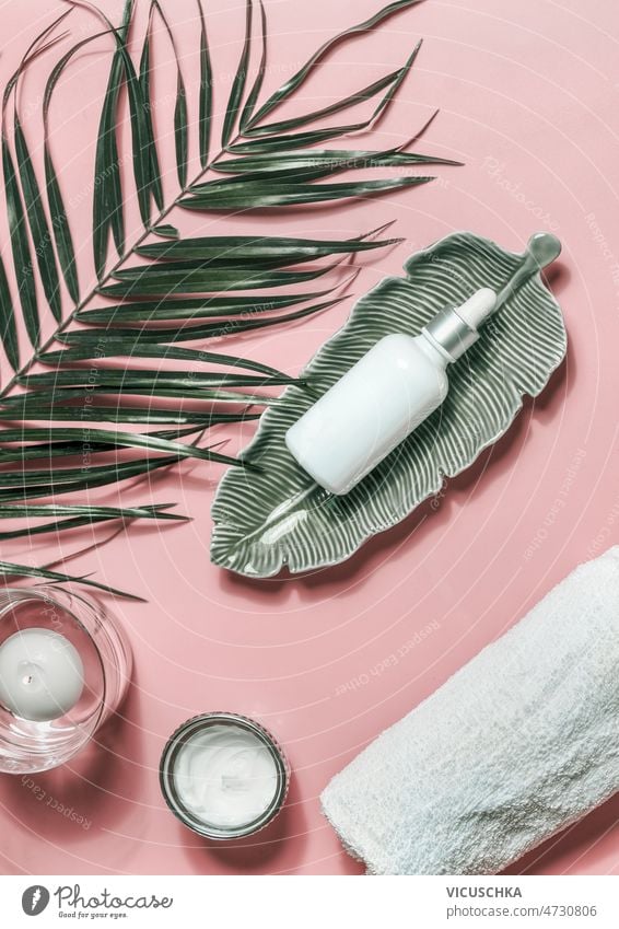 Facial beauty products for skin care.  Cosmetic bottle with pipette, palm leaf, candles and towel at pink background facial healthy natural body care white