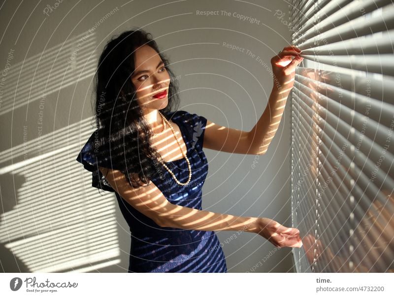 Woman with blinds Dark-haired Long-haired Dress sunny Venetian blinds Stripe room Shadow Jewellery Chain Stand stop open Smiling look Curiosity
