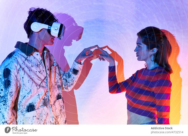 Woman touching finger of man in VR headset couple vr virtual reality cyberspace future metaverse interactive technology explore goggles futuristic studio modern