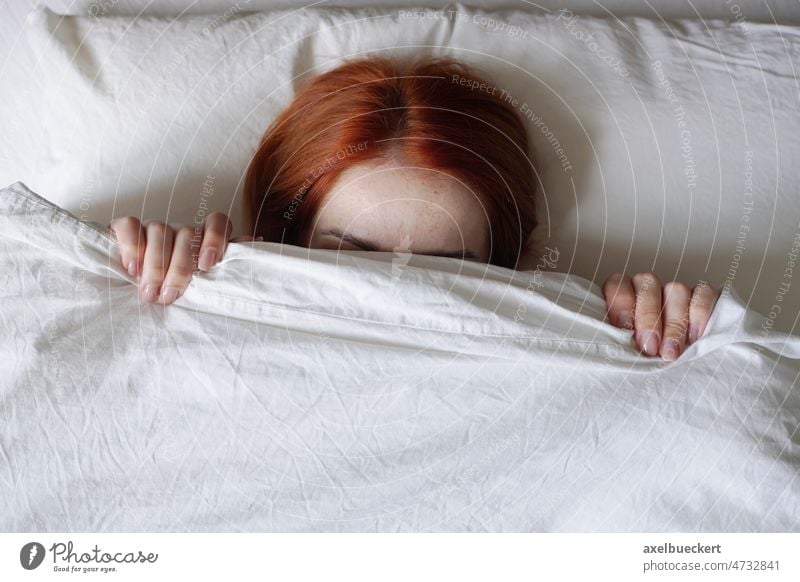 woman hiding face from sunlight under bed cover girl morning waking up refusing get out hide sleep bedcover duvet tired person depression anxiety bedroom indoor