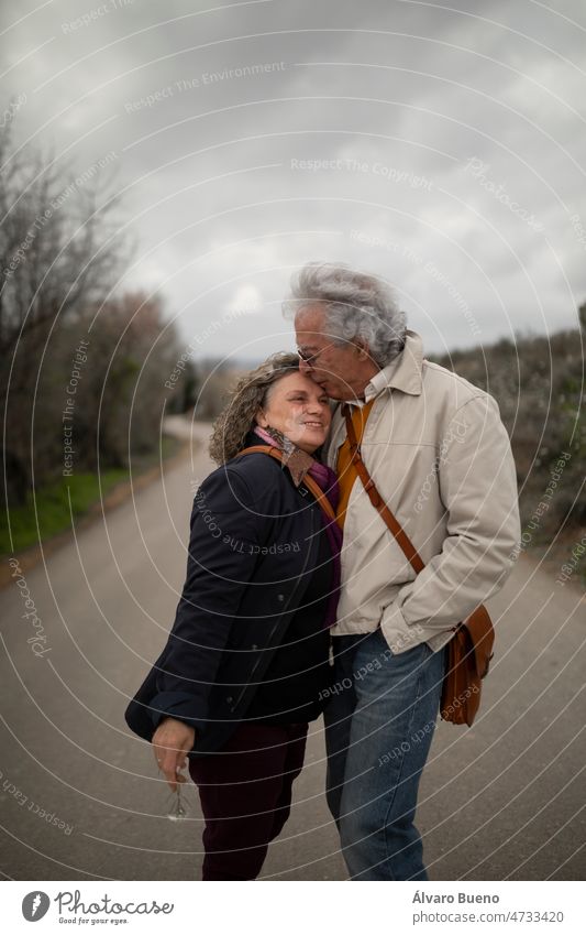 A couple, man and woman, 60 and 70 years old, with gray hair, show affection with a kiss, during a romantic walk in spring, in a rural area of the province of Zaragoza, Aragon, Spain