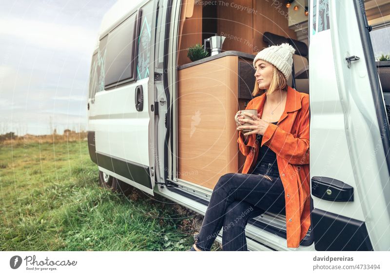 Woman drinking coffee sitting at the door of a campervan woman motorhome holding cup copy space cold thoughtful winter morning serious open door beautiful