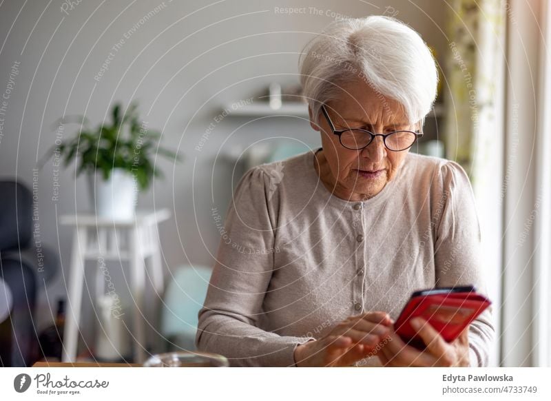 Senior woman using mobile phone at home glasses eyeglasses spectacles alone domestic life elderly female grandma grandmother grey hair house indoors lifestyle