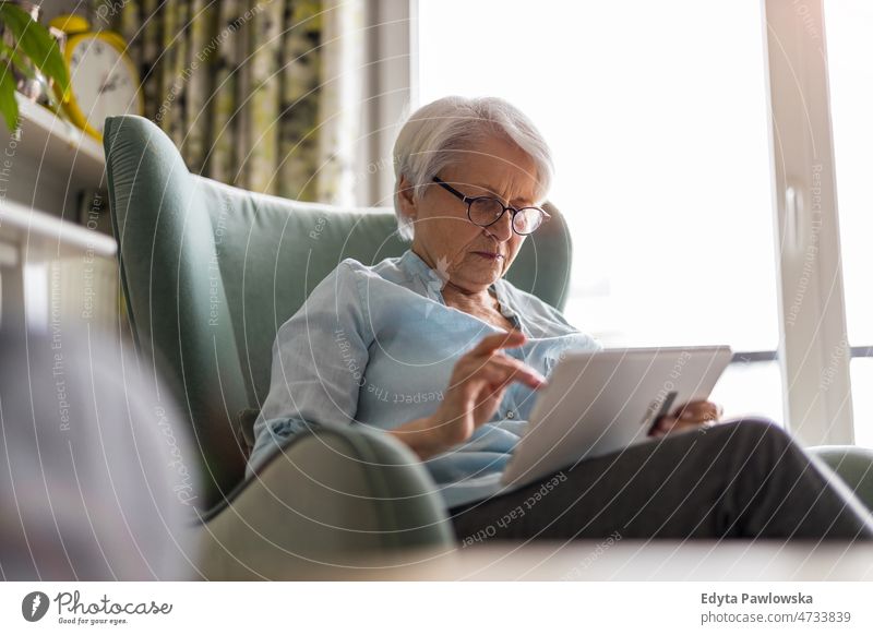 Senior woman using a digital tablet at home online internet modern technology communication connection living room glasses eyeglasses spectacles alone