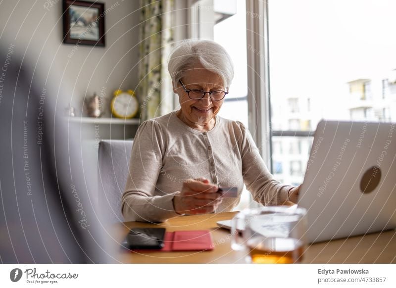 Senior woman doing online shopping on laptop at home glasses eyeglasses spectacles alone domestic life elderly female grandma grandmother grey hair house