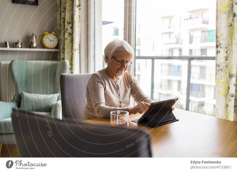 Senior woman using a digital tablet at home online internet modern technology communication connection living room glasses eyeglasses spectacles alone