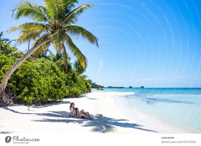 Woman and child lying in the shade of a palm tree on a white sand beach background boy caribbean caucasian coast coastline coconut deserted enjoy enjoying